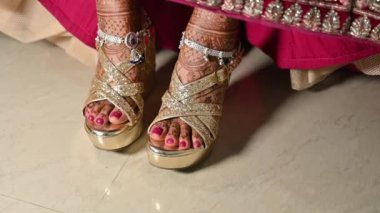 Güzel gelin, gelinlik sandaletlerini bacaklarında gümüş paralarla, gelinlik kınası tasarımı bacaklarında güzel, parlak bir lehenga giyerek gösteriyor. 