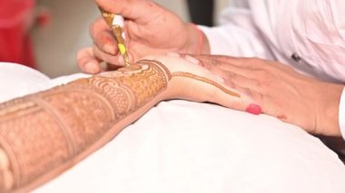 Kadının elinde hazırlanan detaylı ve simetrik çiçek ve geometrik tasarımlara odaklanarak mehndi uygulama sürecinin yakınlaştırılması.