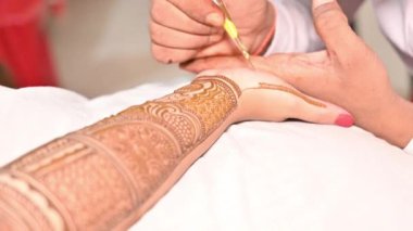 Kadının elinde hazırlanan detaylı ve simetrik çiçek ve geometrik tasarımlara odaklanarak mehndi uygulama sürecinin yakınlaştırılması.