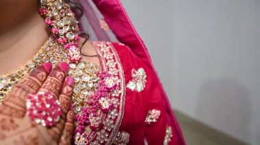 Parlak pembe lehenga (gelinlik) giymiş altın işlemeli bir gelin, elinde geleneksel takılarla tamamlanmış güzel desenli kınasını sergiliyor..