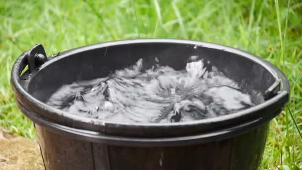 雨水落在桶中 产生水花 雨水滴在水桶中 黑色塑料桶中的水从滴漏的水洒在地板上 液体容器 — 图库视频影像