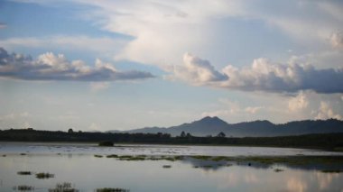 Gölün üzerinde bulutlar, dingin bir göl üzerinde canlı bir günbatımı, suyun üzerinde parıldayan renkli yansımalar, orman ve dağlarla akan bir nehre akan doğal manzara.