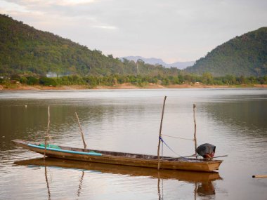 Gölün üzerinde bulutlar, dingin bir göl üzerinde canlı bir günbatımı, suyun üzerinde parıldayan renkli yansımalar, ormanlık ve dağlarla akan bir nehre akan doğal manzara, Mekong Nehri.