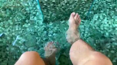 Ayak spa 'sı doğal kaplıcada rahatlar, ayakları lavanta banyosunda, bacaklarını havuzun berrak suyunda sallar. Bronzlaşmış bacaklar ve ayaklar yaz tatilinde dinleniyor.