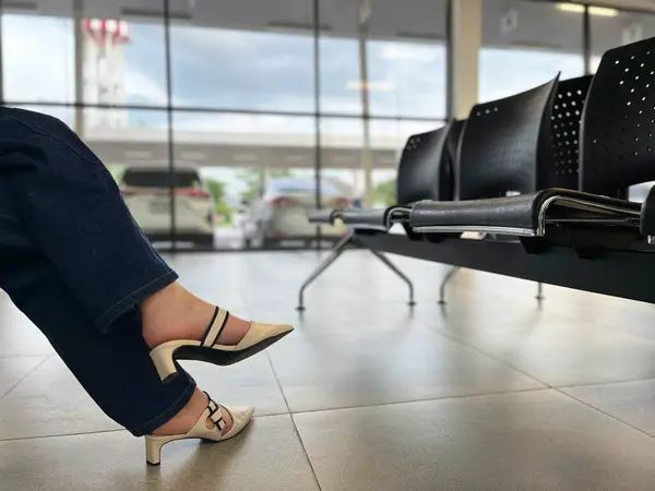 stock image waiting for the flight, a woman sitting in an airport terminal, featuring stylish shoes and a row of modern black chairs, minimalist setting emphasizes the clean design, calm atmosphere, airport