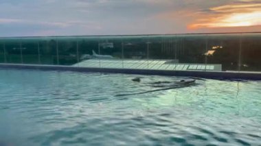 Huzurlu bir çatı sonsuz havuzu çarpıcı bir günbatımının canlı renklerini yansıtır, sakin ve huzurlu bir atmosfer yaratır rahatlama ve lüks seyahat için mükemmel, havuz üzerinde huzurlu bir gün batımı.