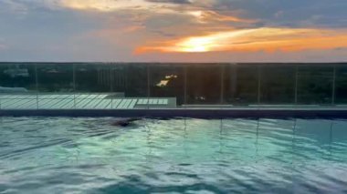 Huzurlu bir çatı sonsuz havuzu çarpıcı bir günbatımının canlı renklerini yansıtır, sakin ve huzurlu bir atmosfer yaratır rahatlama ve lüks seyahat için mükemmel, havuz üzerinde huzurlu bir gün batımı.