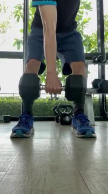 Güçlü ve kararlı bir şekilde dambılı kavrıyor. Arka planda diğer spor malzemelerinin bulanık bir görüntüsü var, dambıl üzerindeki odak noktası ve egzersiz yoğunluğu, fitness