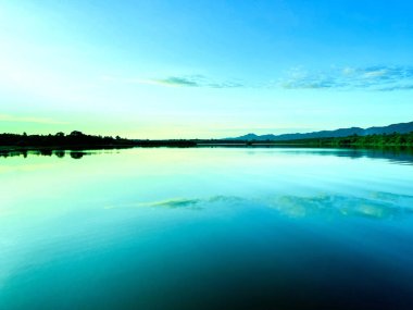 a calm lake at dawn, reflecting the soft hues of the sky on its still surface, silhouette of distant hills and trees frames the horizon, water gently mirroring the serene landscape, sky transitions clipart