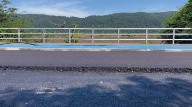 Yol silindiri yeni yerleştirilmiş asfaltı bir yol inşaatına sıkıştırıyor. Sarı patenci yolun pürüzsüz bir bölümünde çalışırken görülüyor, etrafındaki korkuluklar, inşaat mühendisliği...