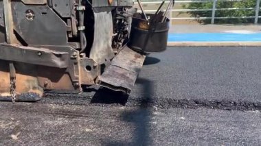 Asfalt kaldırım taşı makinesi yola taze asfalt seriyor. Görüntü makineyi iş başında yakalıyor, yayıcı ekranı ve diğer bileşenleri gösteriyor, pürüzsüz asfalt tabakası, inşaat sahası, sivil