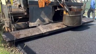 Asfalt kaldırım taşı makinesi yola taze asfalt seriyor. Görüntü makineyi iş başında yakalıyor, yayıcı ekranı ve diğer bileşenleri gösteriyor, pürüzsüz asfalt tabakası, inşaat sahası, sivil
