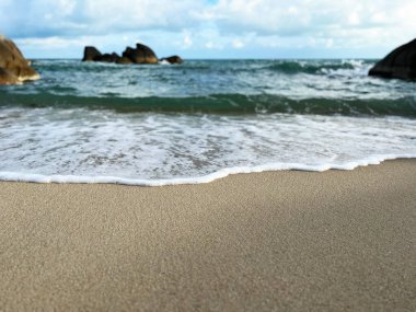 Sahilde dalgalar, kıyıya vuran yumuşak bir okyanus dalgası olan kumlu bir sahil manzarası. Yumuşak köpük, ince kum, huzurlu sahil manzarası, ön planda pürüzsüz kum, nazik okyanus dalgası ile çelişiyor.