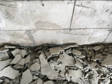 Beton duvar dokusu, beton bloktaki duvarda çatlamış beton alçı ve yere düşen enkaz. Görüntü, inşaat hataları, bina bozulması ve yapısal hasarı vurguluyor
