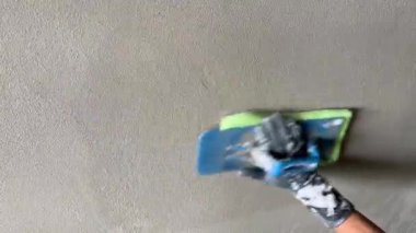 İnşaat işçisi mavi bir malayla duvara sıva yapıyor. Görüntü, inşaatı mükemmel bir şekilde bitirmek için çimentoyu pürüzsüz hale getirme sürecini yakalıyor.