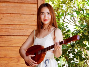 Genç Asyalı bir kadın açık havada akustik bir gitar tutuyor. Müzikal hayat tarzının ve kişisel ifadenin huzurlu anı, gitarlı genç kadın.