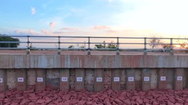 Dayatılmış beton istinat duvarı ve gün batımında bir su deposunun yanında yığın numaraları. Toprak erozyonunu ve seli önlemek için tasarlanmış altyapı yapısı, nehir üzerinde köprü.