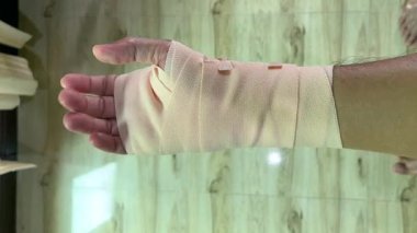 Pembe bir bandaja sarılı yaralı bir el, bir kazadan veya ameliyattan sonra tıbbi bakım ve iyileşme sürecini gösteriyor