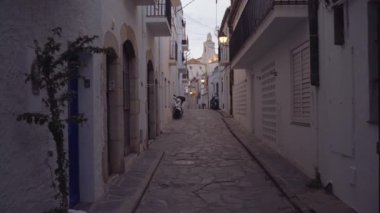 Gün batımında Kadavra 'da sessiz dar bir cadde. Parlak bir sokak lambası ve arka planda kilise var. Park halindeki bir motosiklet kaldırımda, huzurlu atmosferi yakalıyor.