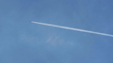 Bir uçak açık mavi gökyüzünü geçerek ardında yavaş yavaş yok olan beyaz bir iz bırakır. Duman zamanla kaybolur ve güzel bir atmosferik etki yaratır.