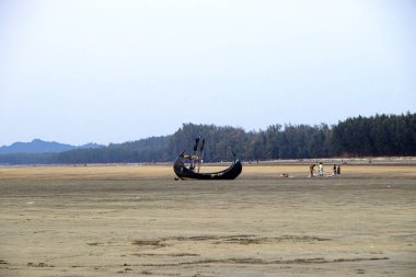 A traditional fishing boat resting on the golden sands of a sea beach in Bangladesh, set against the backdrop of a tranquil blue sky and gentle ocean waves.  clipart