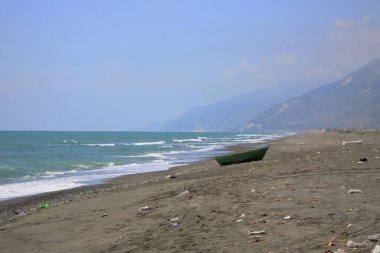 Deniz kenarındaki kumların üzerinde duran yeşil tekne ve etrafındaki çöpler. Dünya çevre günü kavramı fikri.