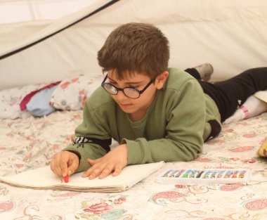 Depremden kurtulan çocuk çadırda resim çiziyor..