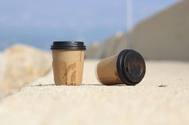 Yere atılmış plastik kapaklı tek kullanımlık karton bardak. Akdeniz limanında yerde kirli kahve fincanı. Dünya Çevre Günü fikri. Tek kullanımlık karton bardağa odaklan. 