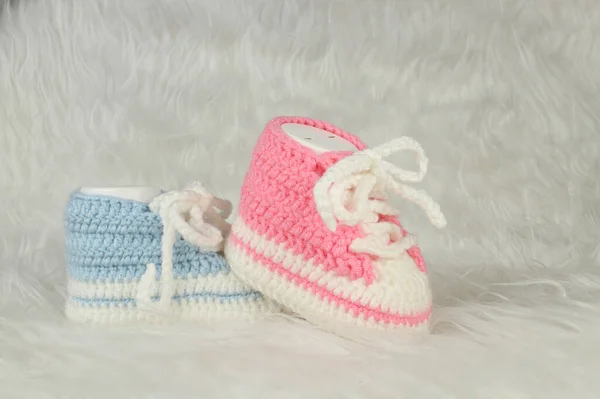 在白色蓬松的毛毯上编织粉红色和蓝色的靴子 性别党的理念 男婴或女婴的第一个步骤 — 图库照片