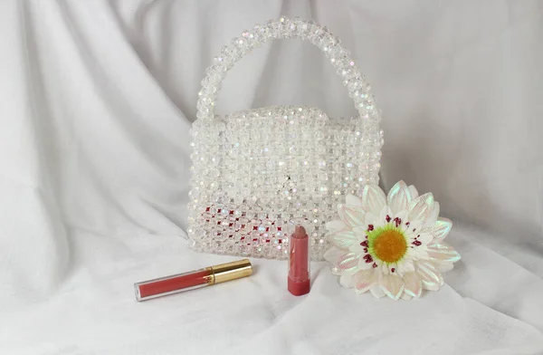 Handmade white purse made with bright beads on gray fabric with makeup tool and fake daisy flower.