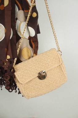 Örgü örülmüş açık bej renkli çanta ve beyaz arka planda kahverengi şal. Dikey çekim. 