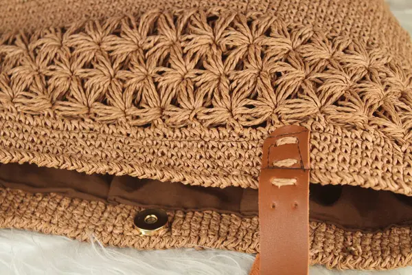 Cream handmade knitted bag on a white fluffy blanket. Close up.