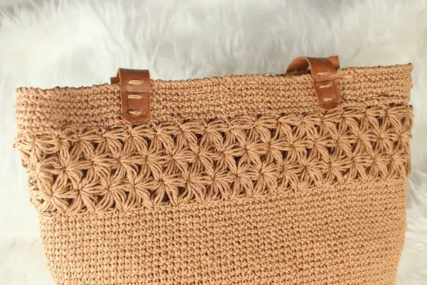 Cream handmade knitted bag on a white fluffy blanket. Close up.