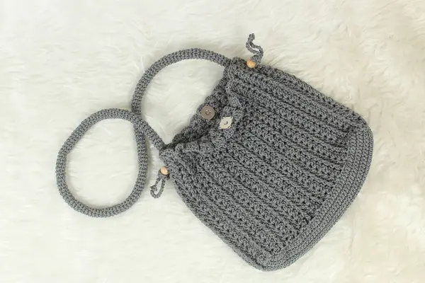 Knitted handmade gray bag on furry white blanket. Top view.