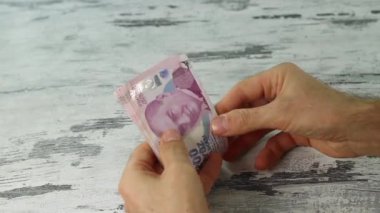Beyaz ahşap masada 200 lira Türk banknotu sayan bir adam. Yakın plan..
