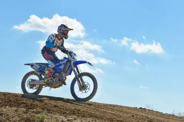 Casarrubios del Monte, Toledo / İspanya - 18 Eylül 2021: Arka planda bulutlu mavi bir gökyüzü ile motosiklet üzerinde duran amatör bir motokros sürücüsünün görüntüsü.