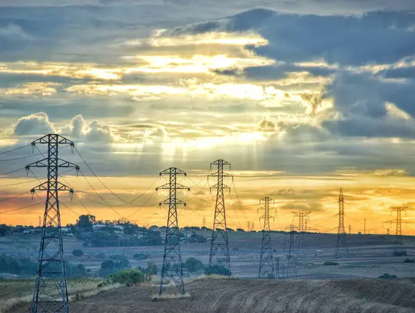 Şafakta güneş ışınlarıyla çarpıcı gökyüzü altında yüksek voltaj direkleri.