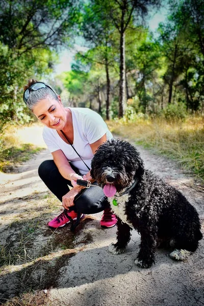 Taşrada İspanyol su köpeğiyle poz veren olgun bir kadın..