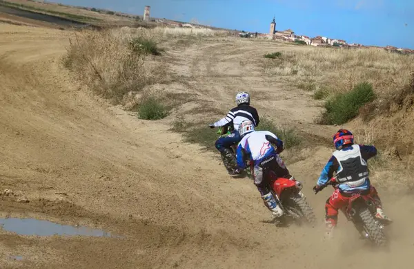 Casarrubios del Monte, Toledo / İspanya - 18 Eylül 2021: Arka planda Casarrubios del Monte, Toledo (İspanya) kasabası kilisesi ve evleri ile bir tur manevrası yapan bir grup amatör motokros motosiklet sürücüsünün görüntüsü.