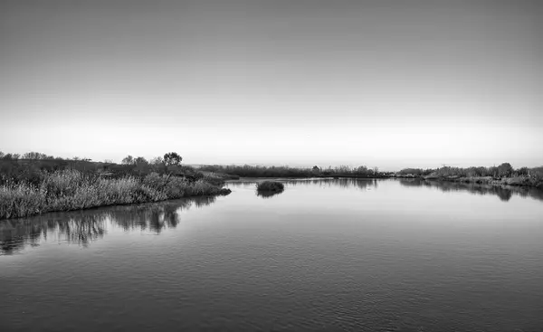 Minimalist black and white landscape of the calm waters of the Tagus River, as it passes through Talavera de la Reina, Spain.