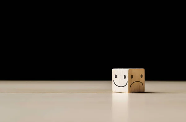Smile face on the bright side and sad face in dark side on the wooden block cube for positive mindset selection. Mental health and emotional state concept, choice satisfaction feedback emotional.