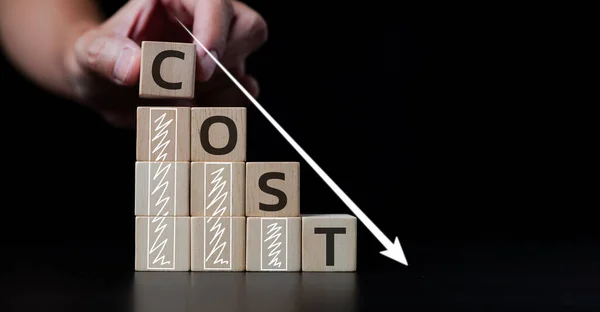 Cost reduction concept. Optimization manufacturing management. Reduce company expenses to maximize profits. Hand placing a wooden cube with the word cost and white downward arrow. Effective business