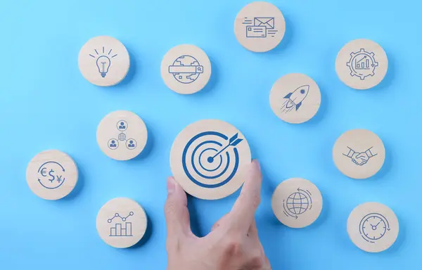 The concept of business goal and marketing target. Man hand holding wooden block with bullseye icon and other business icons. Goal objective strategy plan action, Target success, Achievement company,