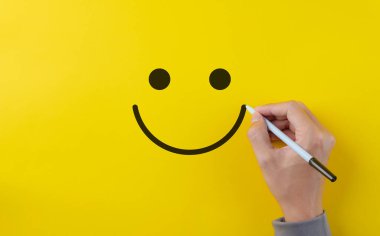 Müşteri memnuniyet değerlendirmesi anket konsepti. Sarı arka plana gülen surat çizmek için kalem kullanıyor. Hizmet ürünü değerlendirme işi, olumlu düşünme, zihinsel sağlık değerlendirmesi,