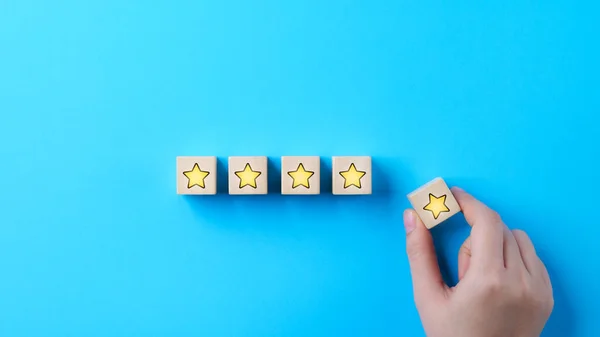 Customer review satisfaction feedback survey concept. Hand put wooden cube block with yellow star icon on blue background. Client questionnaire, Service rating user, Business evaluation, 5, Five star,