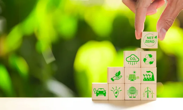 Carbon footprint concept. Hand put wooden cube with net zero icon and green icon on nature background. Net zero and carbon neutral, Carbon emissions, CO2 reduction, Sustainable energy, Climate change,