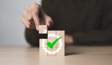 İşadamı eliyle kalite garanti simgesi olan tahta küpü yerleştirdi. Kalite kontrol ve sertifika standart konsepti. ISO hizmet standartlaştırması, Kalite güvencesi ve yönetimi, prim garantili ürün,