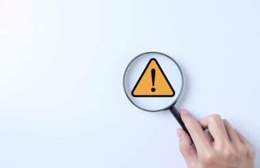 Uyarı sistemi konsepti. Büyüteç sarı üçgen uyarı işaretine odaklanmış. Bildirim hatası ve bakım, siber suç ve virüs, kötü niyetli yazılım, siber güvenlik savunmasızlığı,