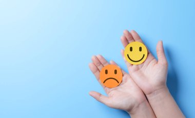 Akıl Sağlığı Günü konsepti. Mutlu ve Üzgün Duygular Simgeleri arasında seçim yapmak. Eller iki yuvarlak simgeyi kaldırıyor, biri gülümsüyor ve biri üzgün, pozitif ve negatif duygular arasındaki seçimi simgeliyor..