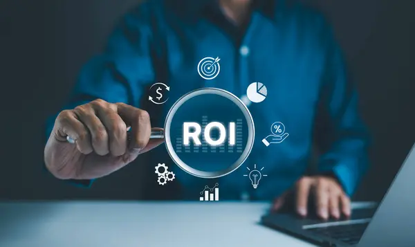 Yatırımın Dönüşü (ROI) Kavramının Analizi Yapılıyor. Elinde ROI ve çeşitli finansal simgelerle birlikte büyüteç tutan işadamı, yatırım ve mali performans analizinin geri dönüşünü temsil ediyor.